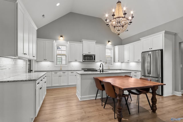 kitchen with appliances with stainless steel finishes, a sink, a chandelier, white cabinets, and high vaulted ceiling