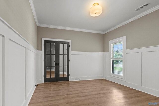 empty room featuring a decorative wall, french doors, ornamental molding, a wainscoted wall, and wood finished floors