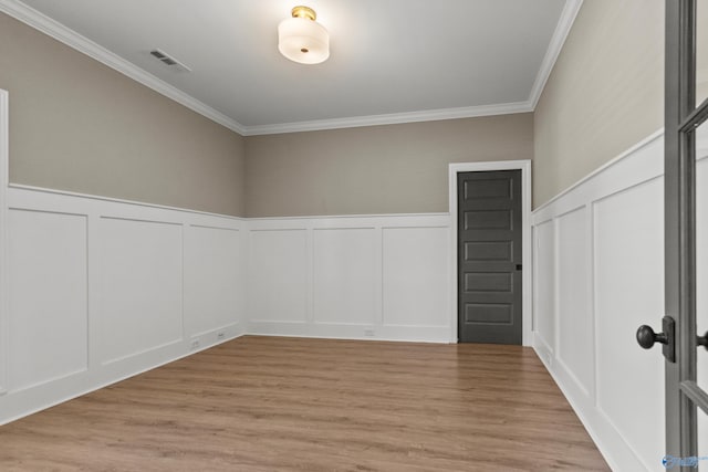 spare room with a decorative wall, crown molding, light wood-type flooring, and wainscoting