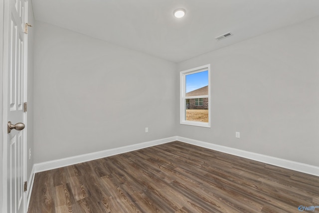 empty room with dark wood-type flooring, visible vents, and baseboards