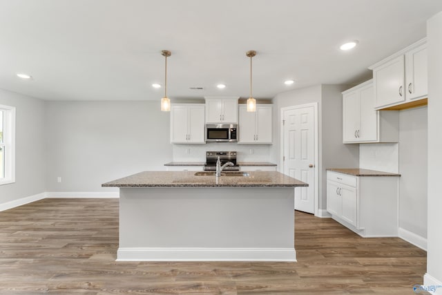 kitchen featuring appliances with stainless steel finishes, dark stone countertops, a kitchen island with sink, and white cabinets