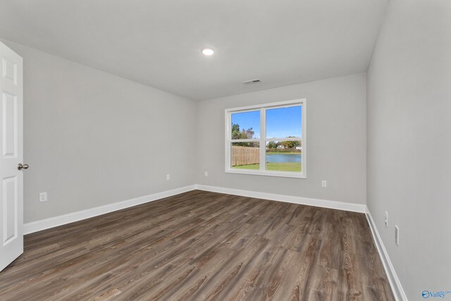 empty room with dark wood-style flooring, visible vents, and baseboards