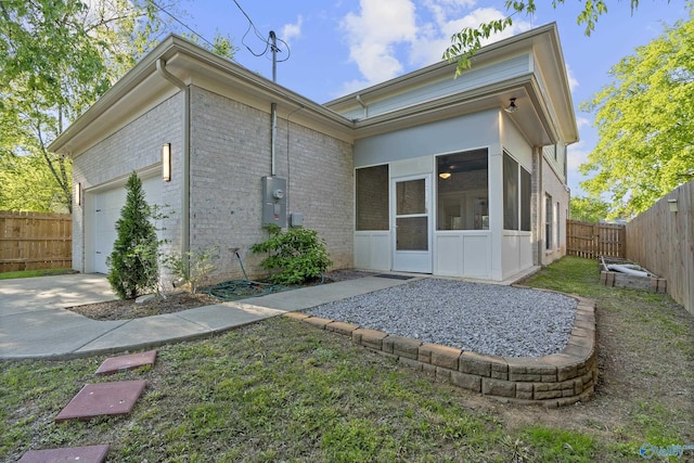 rear view of property featuring concrete driveway, a fenced backyard, an attached garage, brick siding, and a sunroom