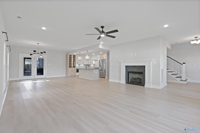 unfurnished living room with a sink, baseboards, ceiling fan with notable chandelier, and a fireplace