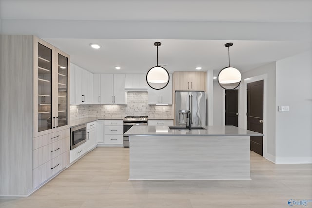 kitchen featuring backsplash, a sink, a kitchen island with sink, glass insert cabinets, and appliances with stainless steel finishes