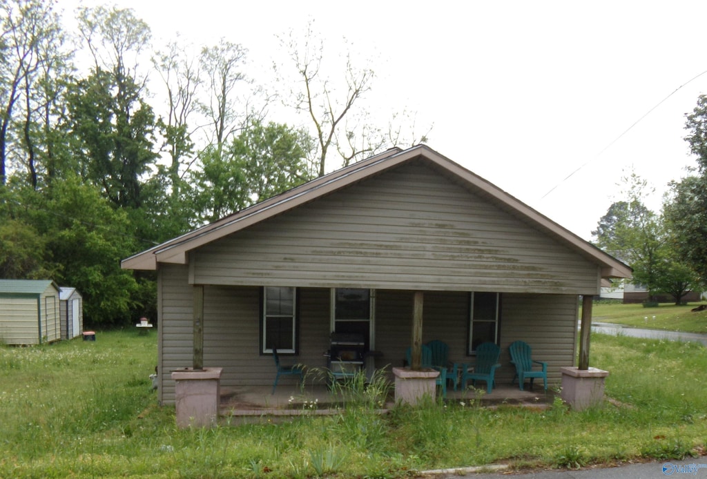 back of house featuring a porch, a storage unit, and an outbuilding