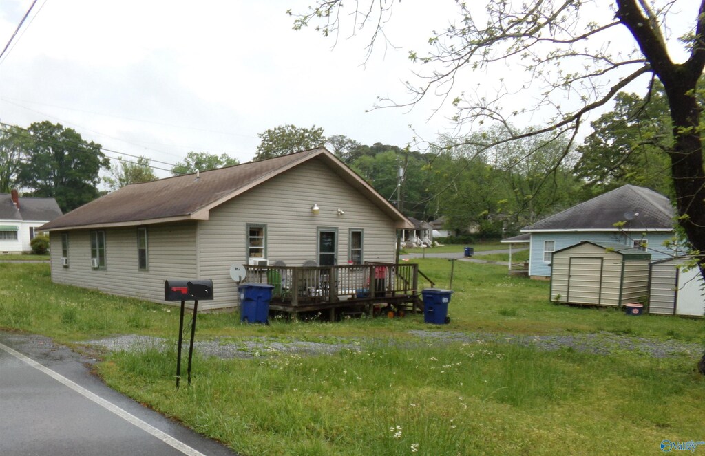 view of property exterior with an outdoor structure, a lawn, a deck, and a storage unit