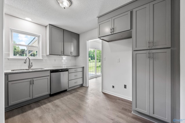 kitchen with a sink, dishwasher, a textured ceiling, gray cabinets, and light wood-style flooring