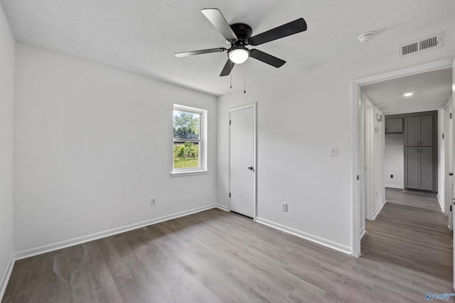 unfurnished bedroom with baseboards, a textured ceiling, visible vents, and wood finished floors