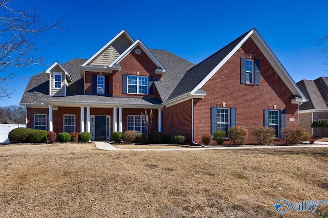 view of front of house with brick siding, covered porch, a front lawn, and fence