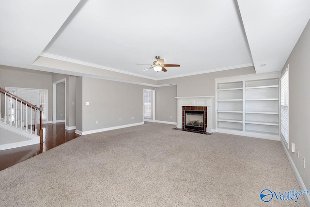 unfurnished living room with baseboards, carpet, a tiled fireplace, stairs, and a ceiling fan