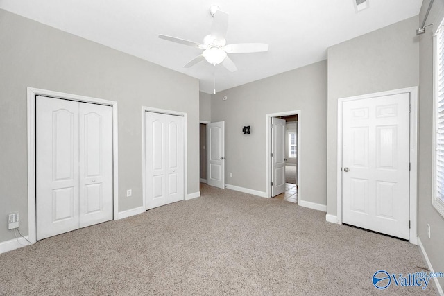 unfurnished bedroom featuring baseboards, a ceiling fan, multiple closets, and carpet floors