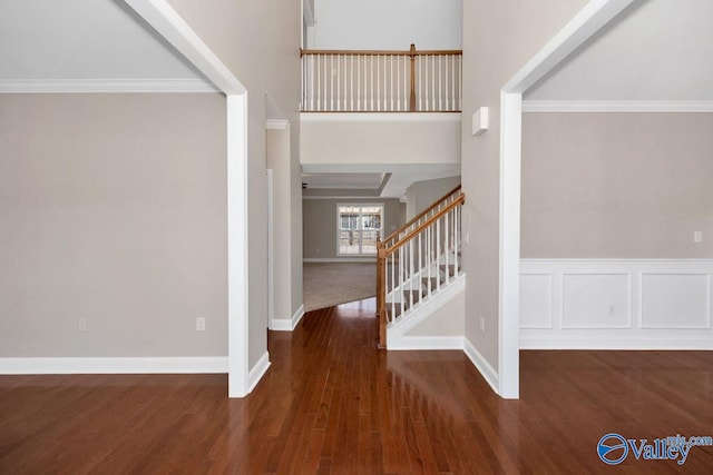 foyer entrance featuring crown molding, baseboards, stairway, wainscoting, and wood finished floors