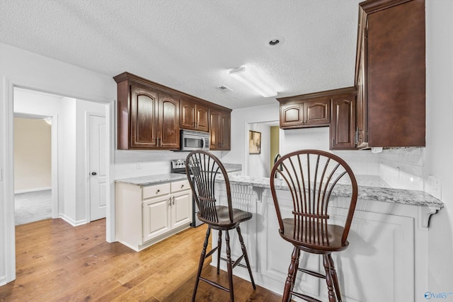 138 Spring Farm Rd, Huntsville, AL 35811 - kitchen featuring stainless steel microwave, light wood-style floors, a breakfast bar area, dark brown cabinets, and a textured ceiling