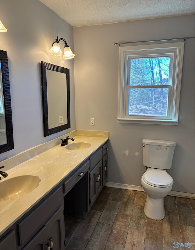 full bath featuring double vanity, toilet, wood finished floors, a textured ceiling, and a sink