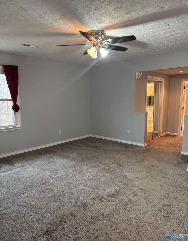 carpeted empty room featuring ceiling fan, a textured ceiling, visible vents, and baseboards