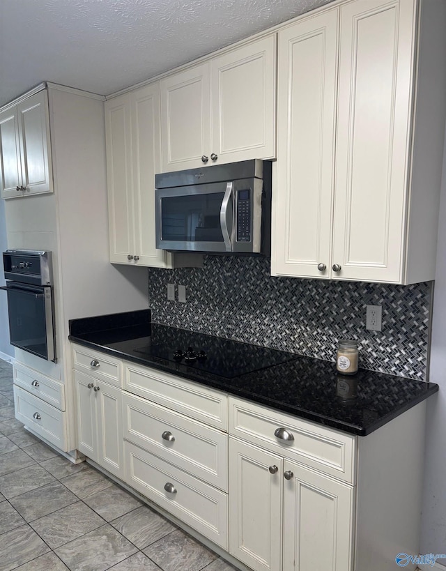 kitchen with wall oven, black electric cooktop, white cabinetry, backsplash, and stainless steel microwave