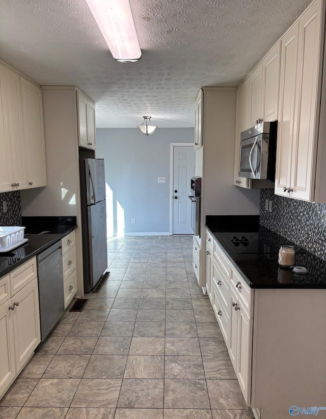 kitchen with stainless steel appliances, tasteful backsplash, dark countertops, and white cabinets