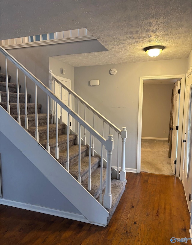 stairs featuring a textured ceiling, baseboards, and wood finished floors