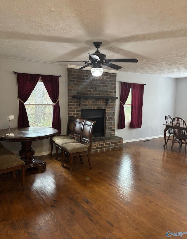 living area with wood-type flooring, visible vents, a brick fireplace, ceiling fan, and baseboards