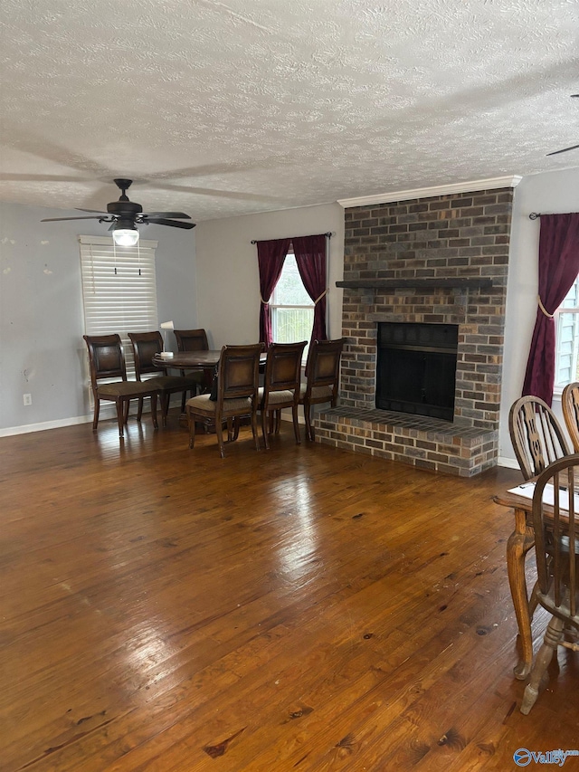 dining room with a textured ceiling, a ceiling fan, baseboards, a brick fireplace, and hardwood / wood-style floors