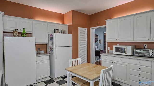 kitchen with white appliances, a toaster, light floors, and white cabinetry