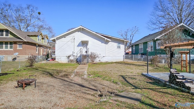 back of property featuring an outdoor fire pit, fence, and a lawn