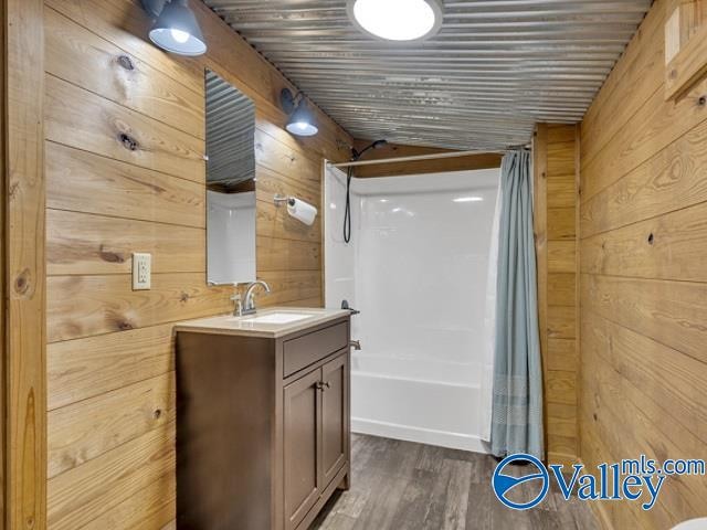 bathroom featuring vanity, shower / bathtub combination with curtain, wood-type flooring, and wood walls
