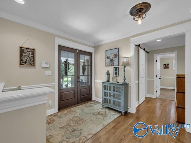 foyer entrance with ornamental molding, hardwood / wood-style floors, a barn door, and french doors