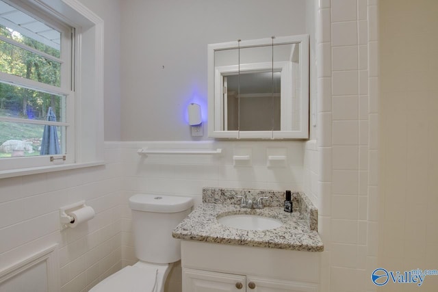 bathroom with vanity, toilet, and tile walls