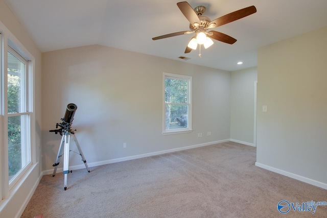 spare room with lofted ceiling, a wealth of natural light, light colored carpet, and ceiling fan