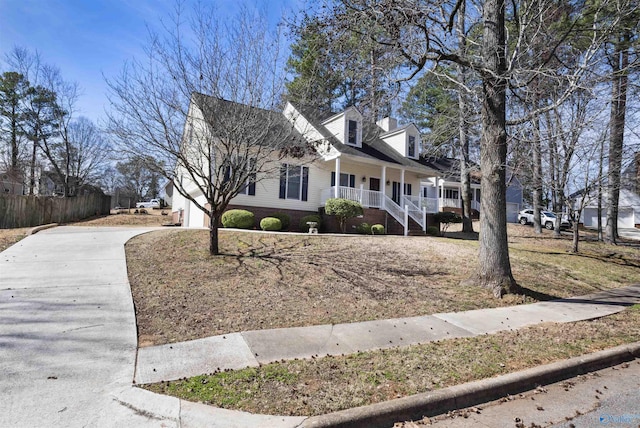 cape cod house featuring covered porch, concrete driveway, and fence