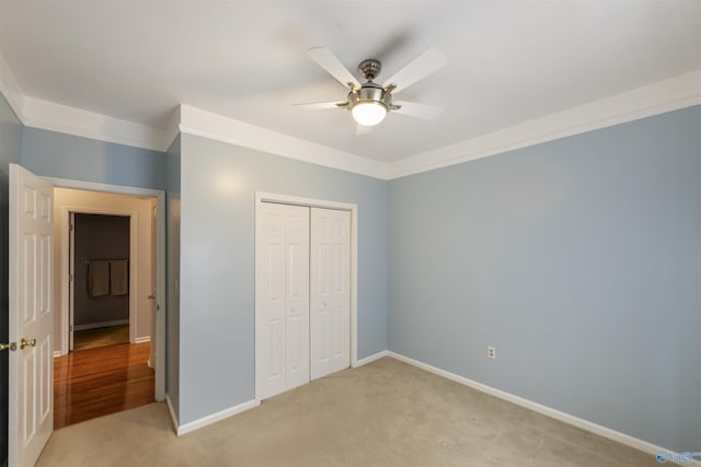 unfurnished bedroom featuring baseboards, ceiling fan, a closet, light carpet, and crown molding