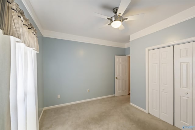 unfurnished bedroom with crown molding, baseboards, light colored carpet, a closet, and a ceiling fan