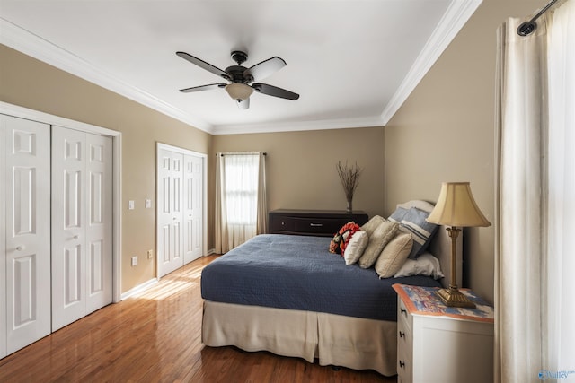 bedroom with multiple closets, ornamental molding, a ceiling fan, wood finished floors, and baseboards