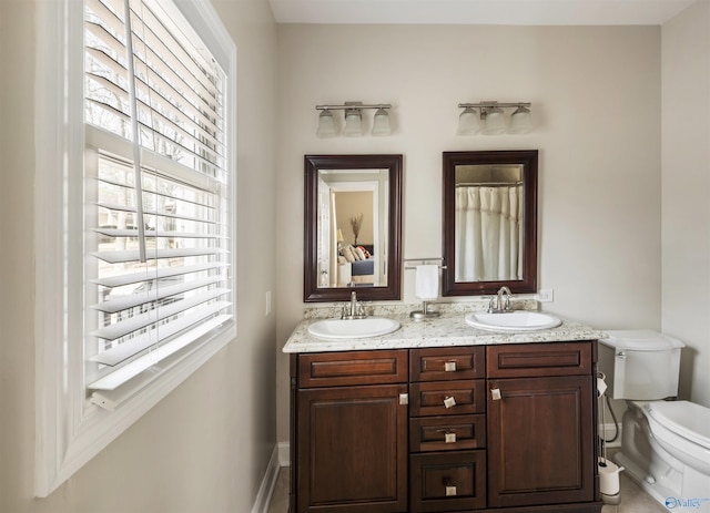 bathroom featuring a sink, baseboards, toilet, and double vanity