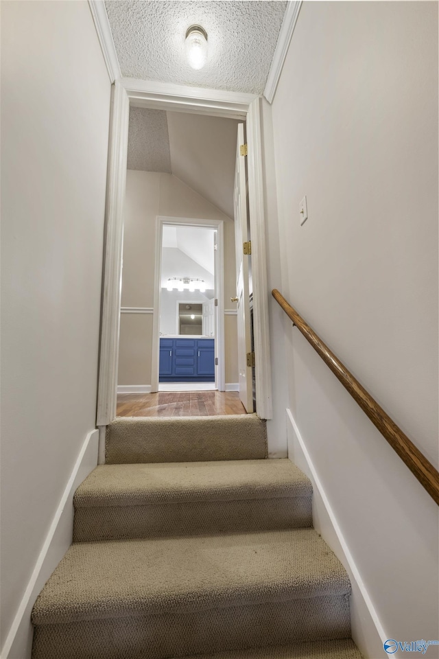 stairs featuring lofted ceiling, wood finished floors, and a textured ceiling