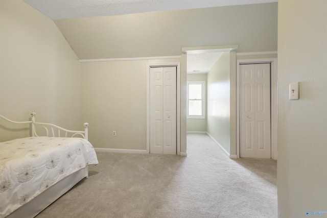 unfurnished bedroom with light colored carpet, two closets, baseboards, and vaulted ceiling