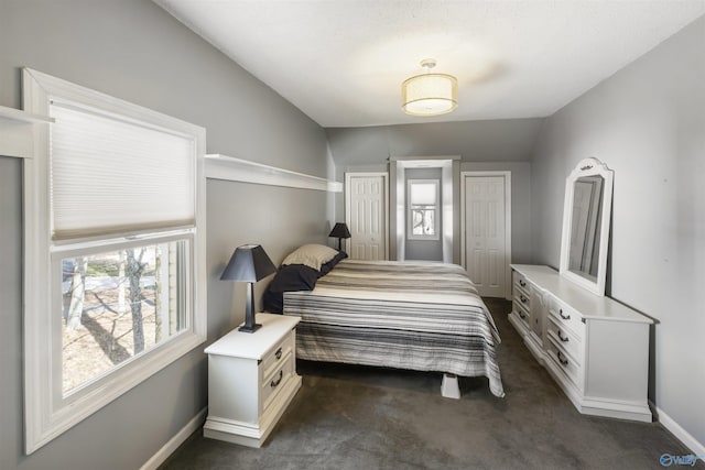 bedroom with dark colored carpet, vaulted ceiling, baseboards, and two closets