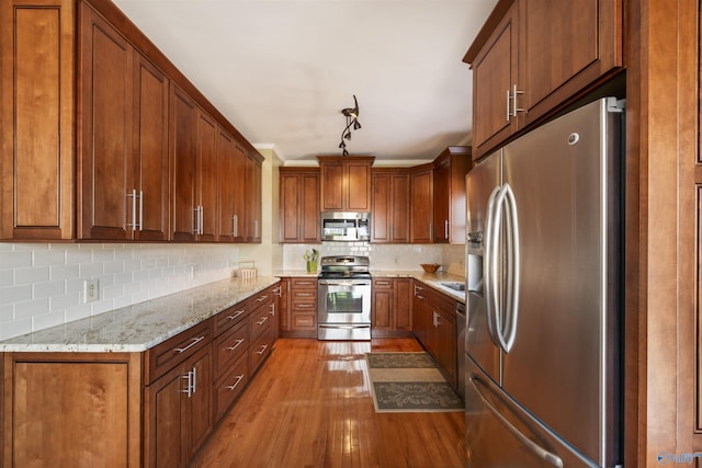 kitchen with light stone counters, brown cabinetry, light wood-style flooring, stainless steel appliances, and decorative backsplash