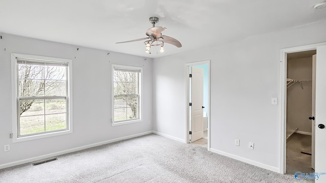 unfurnished bedroom featuring a walk in closet, light colored carpet, visible vents, ensuite bath, and baseboards