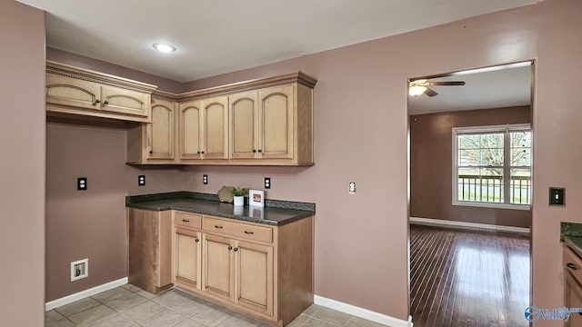 kitchen featuring dark countertops, baseboards, cream cabinetry, and a ceiling fan