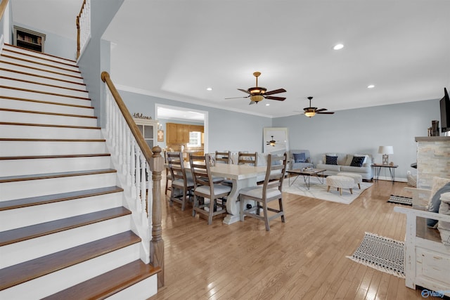 dining room featuring light wood-type flooring, ornamental molding, ceiling fan, and a fireplace