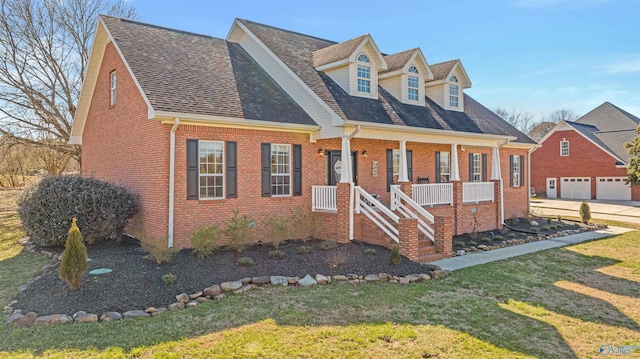 new england style home with covered porch, a garage, and a front lawn