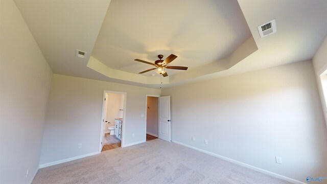 unfurnished bedroom featuring connected bathroom, a tray ceiling, light colored carpet, and ceiling fan