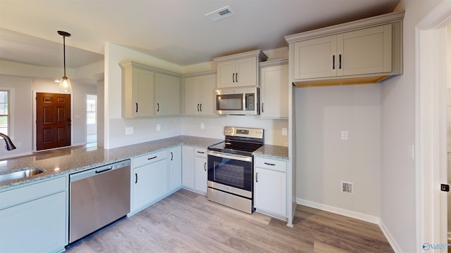 kitchen featuring stainless steel appliances, light stone countertops, hanging light fixtures, and light hardwood / wood-style floors