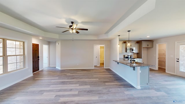 kitchen with light hardwood / wood-style flooring, appliances with stainless steel finishes, kitchen peninsula, pendant lighting, and dark stone counters