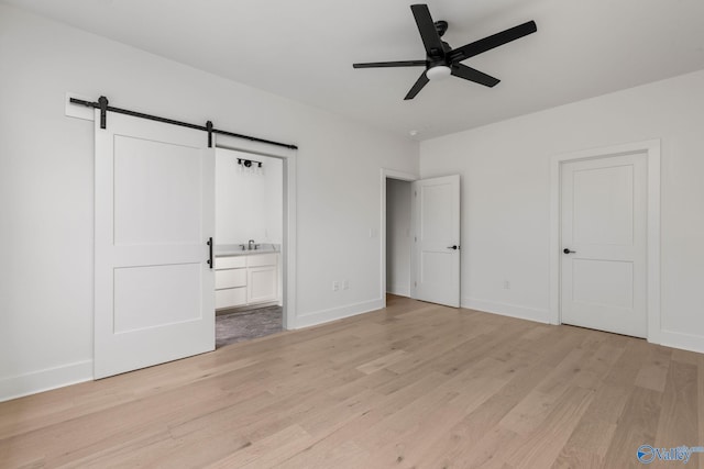 201 Fame Ave, Tuscumbia, AL 35674 - unfurnished bedroom featuring light wood-type flooring, a barn door, a sink, baseboards, and connected bathroom
