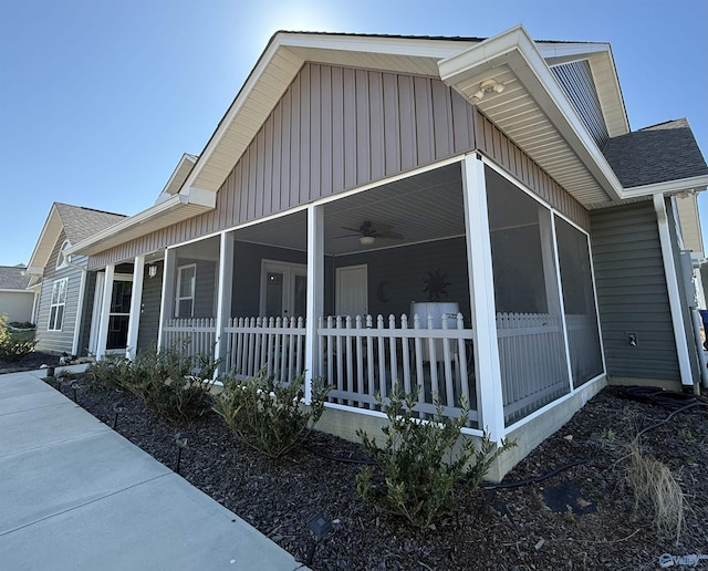 view of home's exterior with board and batten siding, a sunroom, roof with shingles, and fence