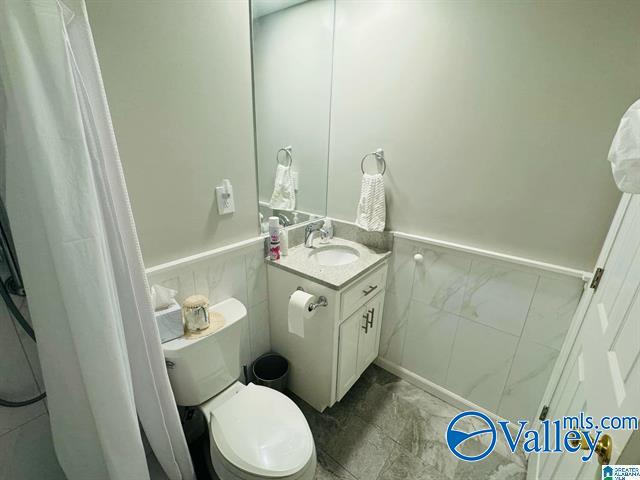 bathroom featuring vanity, toilet, and tile walls